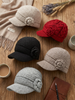 Knitted hats with floral details on a wooden surface with a scarf and coffee cup.