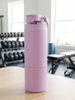 Pink water bottle with a purple cap on a wooden surface in a gym setting